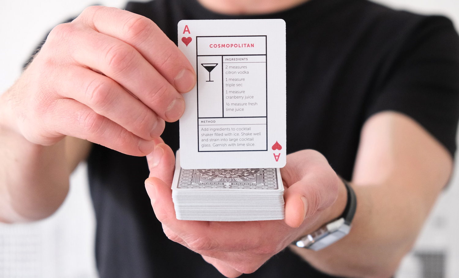 Hands holding up a deck of Cocktail Cards with Cosmopolitan card showing