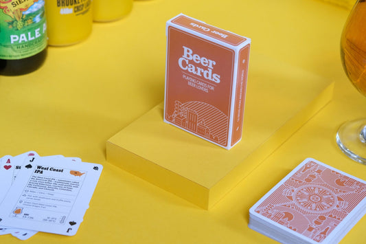 Beer-themed playing cards on a yellow surface with a glass of beer and beer bottles.