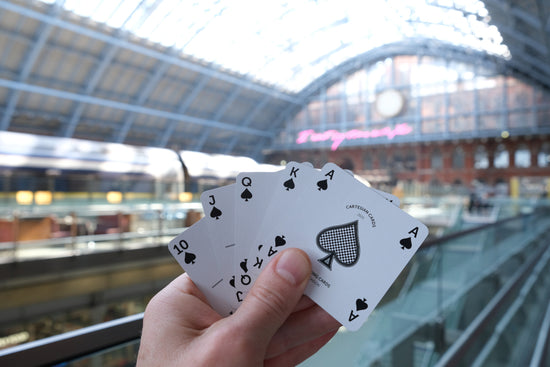 A hand holding a spades royal flush in front of the Eurostar terminal at London St Pancras train station