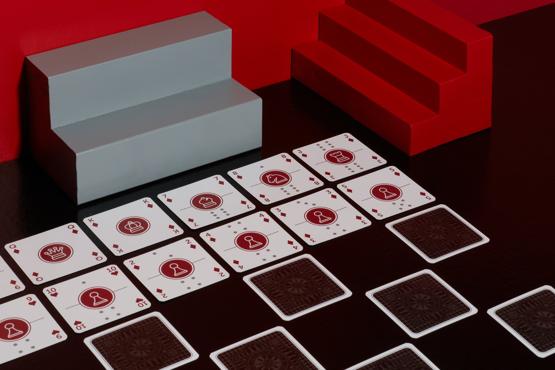A deck of One Deck Game Cards playing cards laid out to play chess with red and grey geometric objects